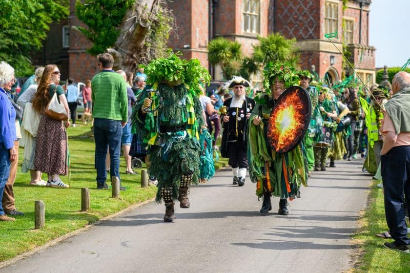 Performers dressed in elaborate Green Man costumes and a traditional town crier lead a vibrant procession through the grounds of The Burley Manor in Burley, Hampshire, during the New Forest Green Man Parade 2026. This community celebration highlights local folklore and the arrival of spring through music, dance, and colorful seasonal pageantry. #newforest #greenmanparade #jerryfennerphotography #newforestphotographer #folklore #burleymanor