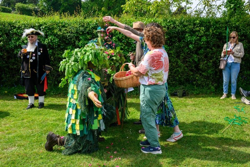 During the New Forest Green Man Parade 2026 in Burley, Hampshire, participants celebrate the arrival of the Green Man by scattering flower petals over him. The tradition, supported by local businesses like New Forest Cider, honours the folklore spirit of the forest, while a town crier observes the colourful festivities in the background.#newforestgreenmanparade#burley#hampshire#folklore#jerryfennerphotography#newforestphotographer