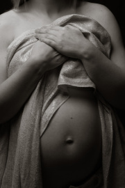 A black and white portrait of a pregnant woman, her hands protectively covering her chest and baby bump. The soft, textured fabric adds a touch of elegance to this intimate moment.