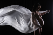 A stunning maternity portrait. A woman in her third trimester poses with a flowing white fabric, highlighting the beauty of pregnancy.