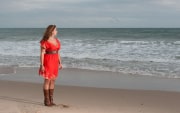 A woman stands contemplatively by the shoreline, wearing a vibrant red dress paired with leather boots. The soft, overcast daylight highlights the quiet mood as she gazes towards the horizon in this reflective portrait.#jerryfennerphotography #beachportrait #naturalphotography #coastalportraits #editorialstyle #portraitmood #outdoorportrait #beachstyle #quietmoment #reflectiveportrait #portraitinspiration
